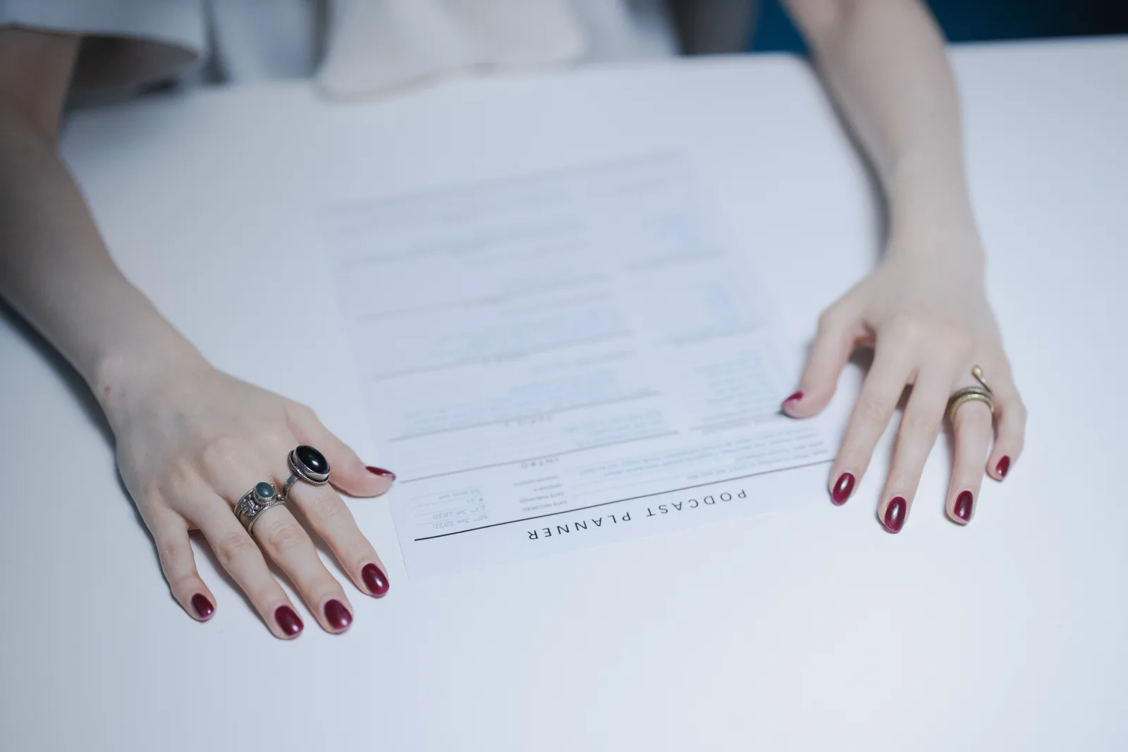Close-up of hands with rings holding a podcast planner on a white table. Sample podcast quotes and the template behind them without the jargon