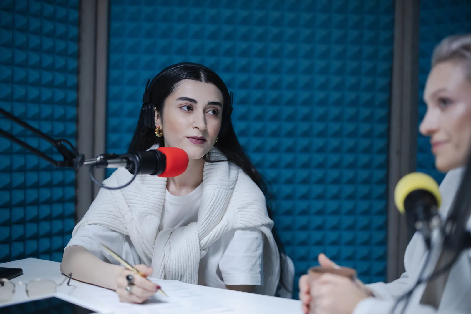 Two women engaged in a podcast recording with professional microphones, soundproof studio. Why Los Angeles and New York podcast studio rates run higher