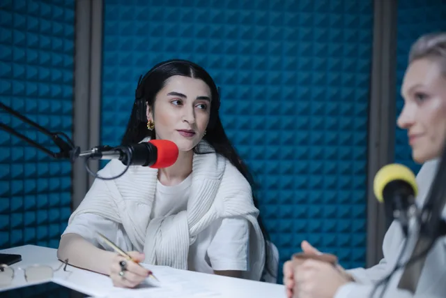 Two women engaged in a podcast recording with professional microphones, soundproof studio. Why Los Angeles and New York podcast studio rates run higher